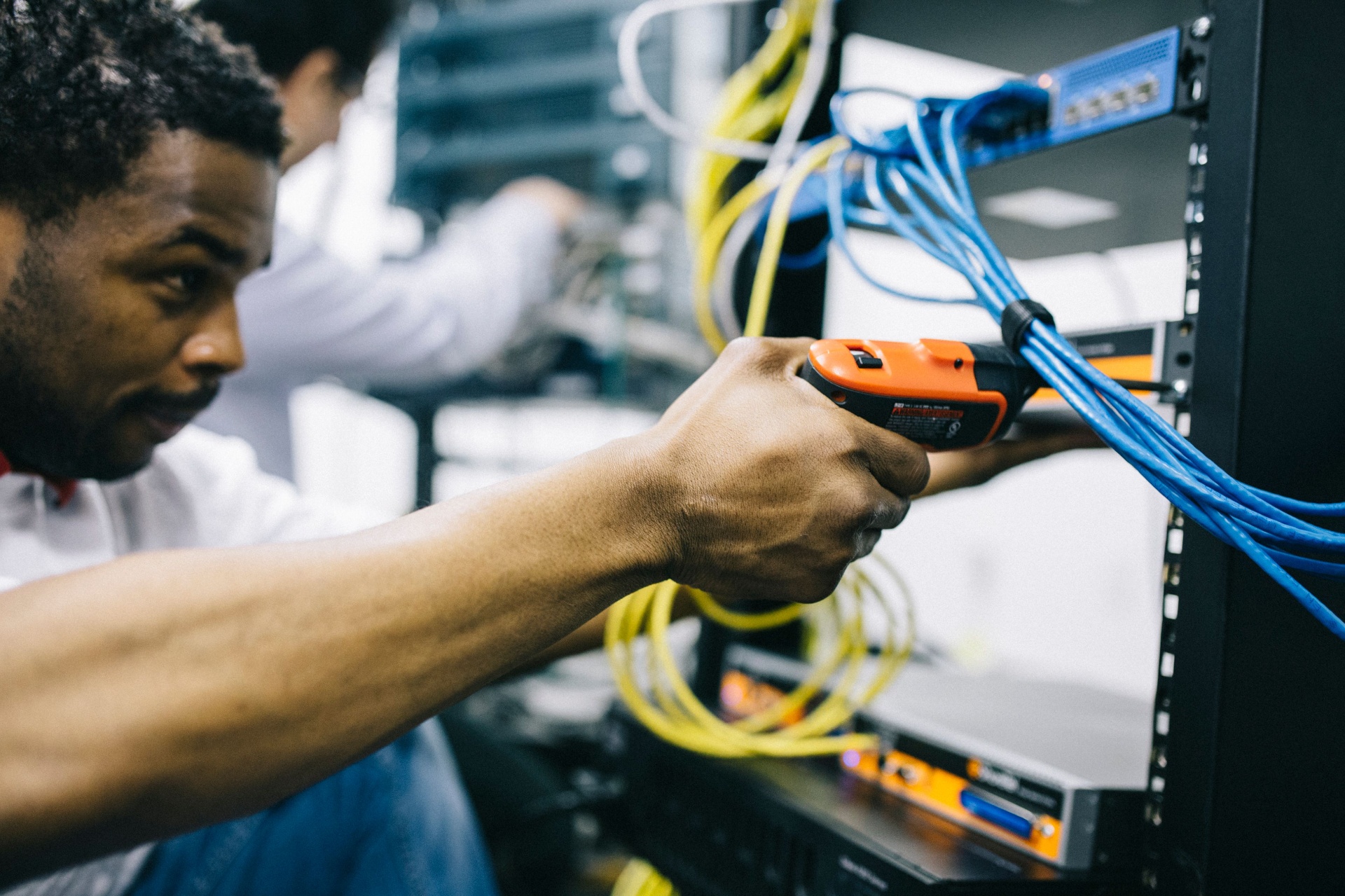Técnico Vale IT Solutions realizando manutenção de infraestrutura de rede em rack corporativo.