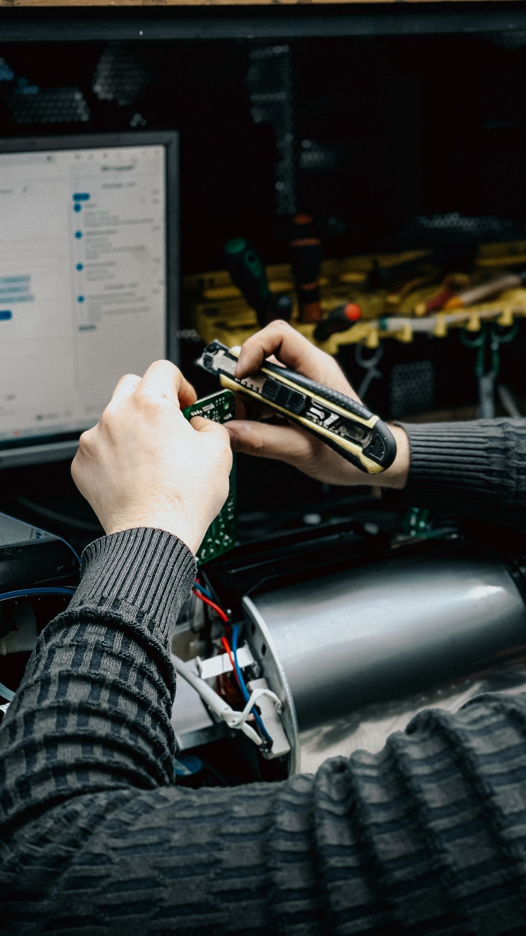 Manutenção especializada de placa eletrônica em bancada, com ferramentas e computador de apoio.