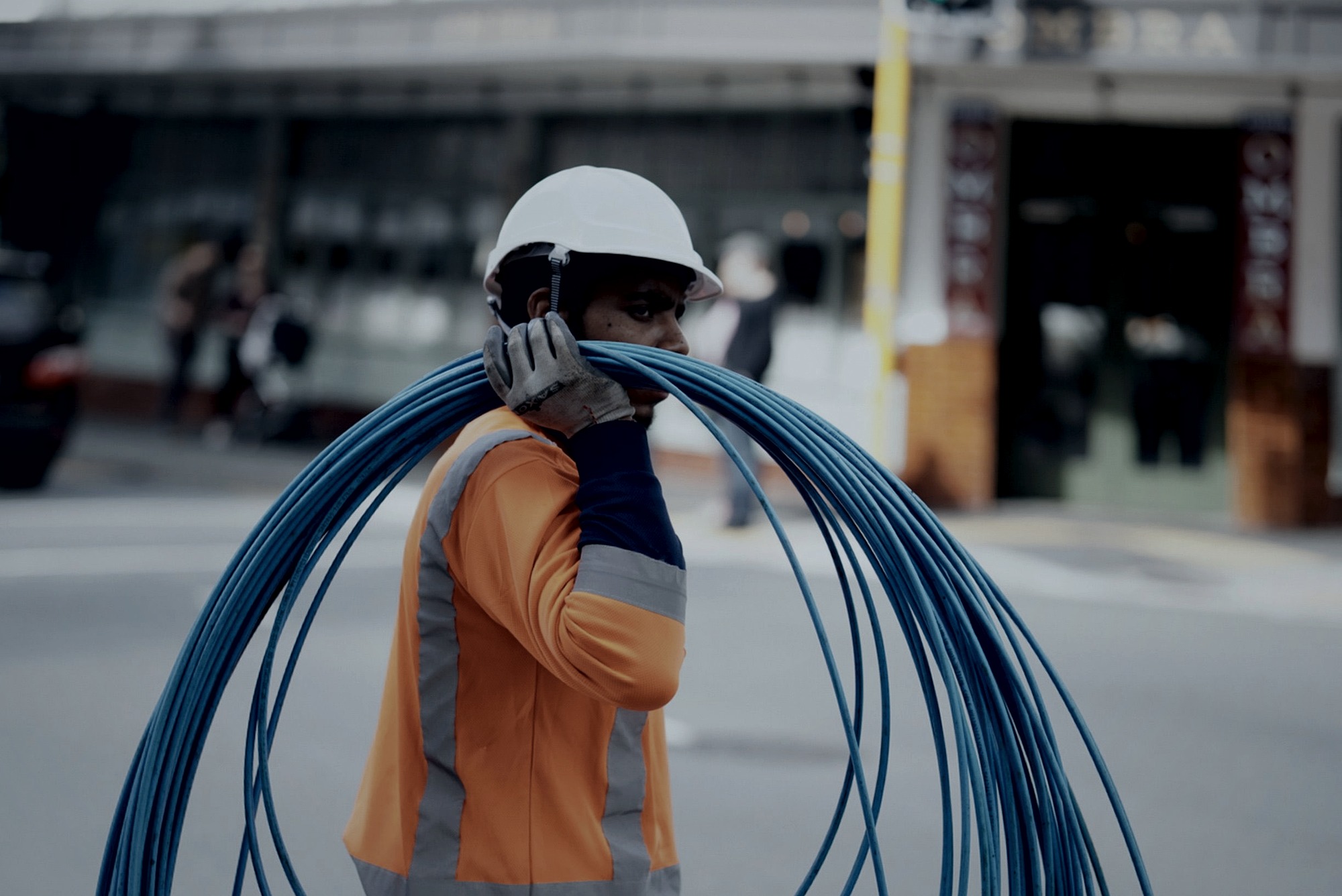 Profissional de manufatura com capacete e uniforme de alta visibilidade carregando cabeamento estruturado — operação industrial atendida pela Vale IT Solutions.